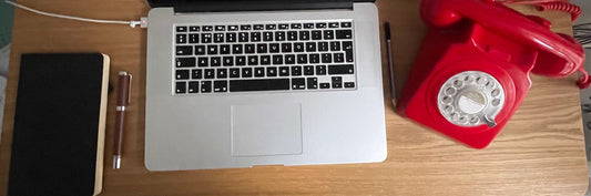 Writers desk with a computer, phone, and writing pad on it.